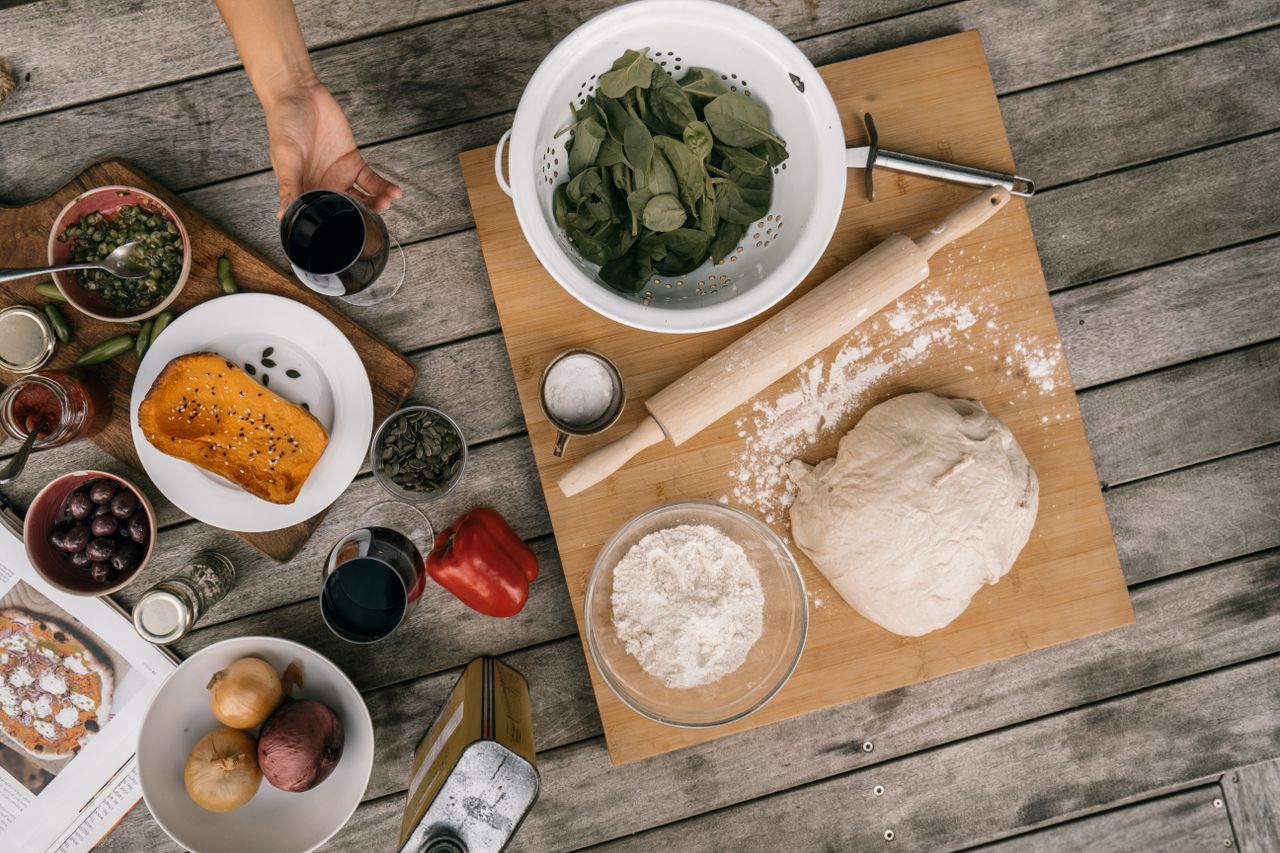 An overhead view of ingredients and tools for making homemade pizza on a wooden table.